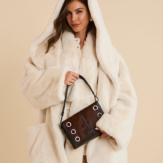 Woman in a white fur coat holding a brown handbag with a beige background