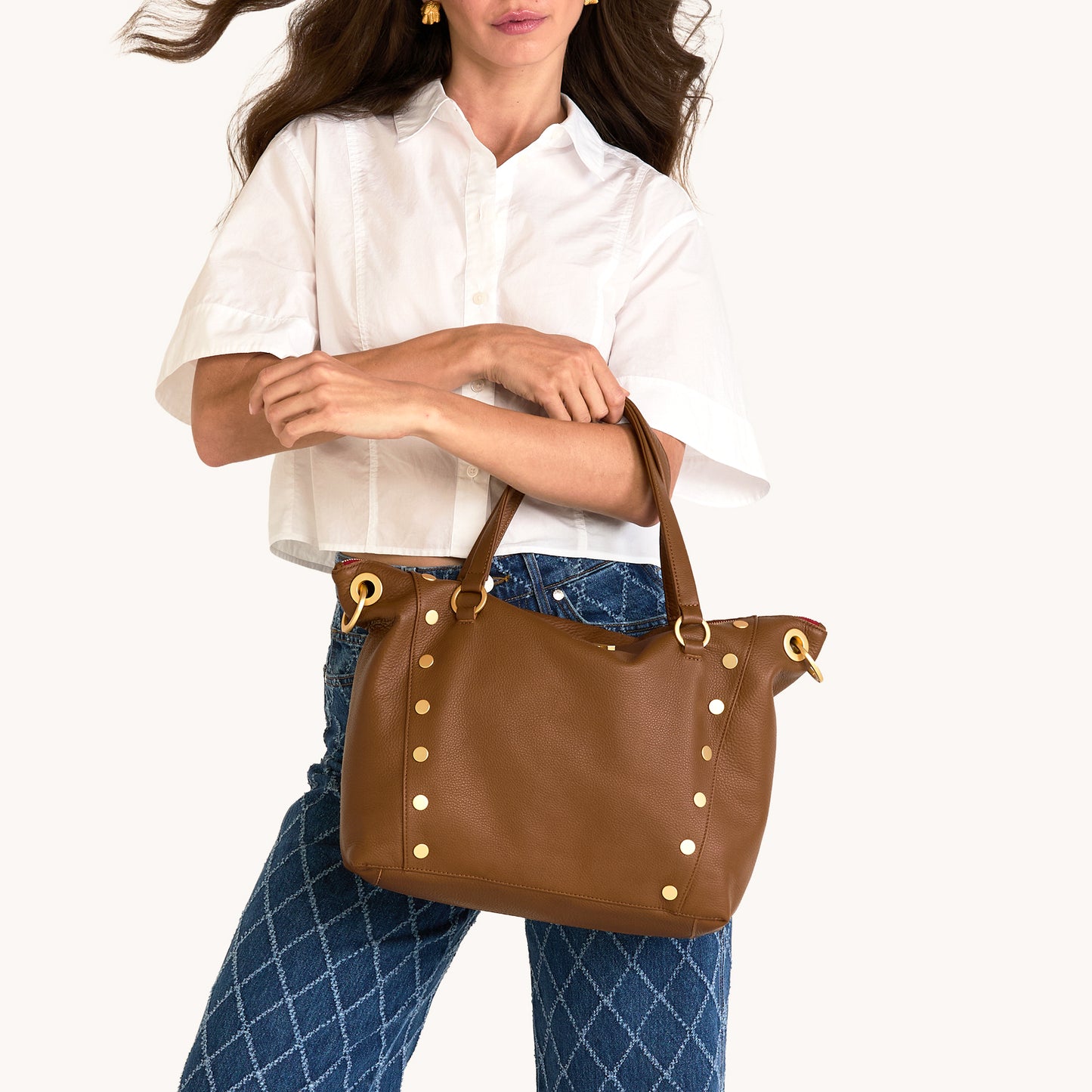 Woman holding a brown leather handbag with gold accents on a white background