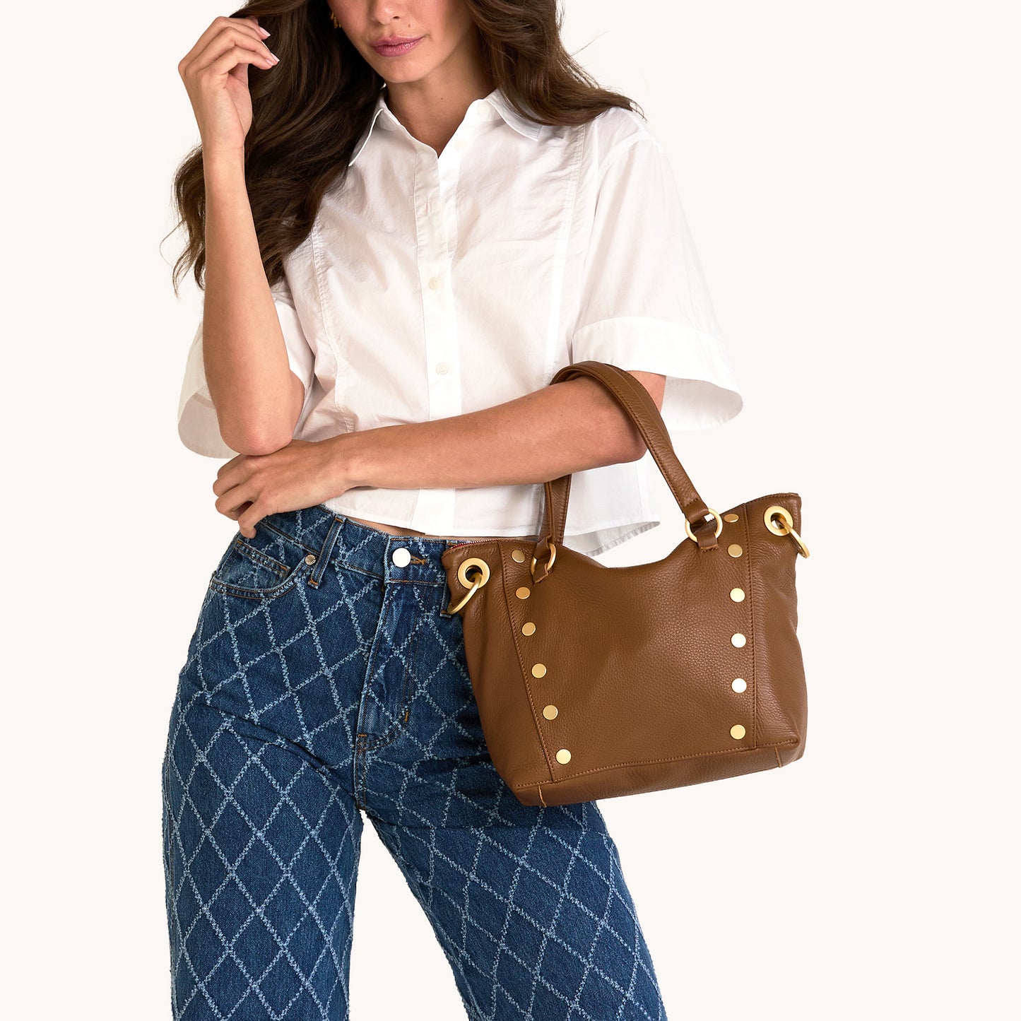 Woman holding a brown handbag with gold accents against a white background