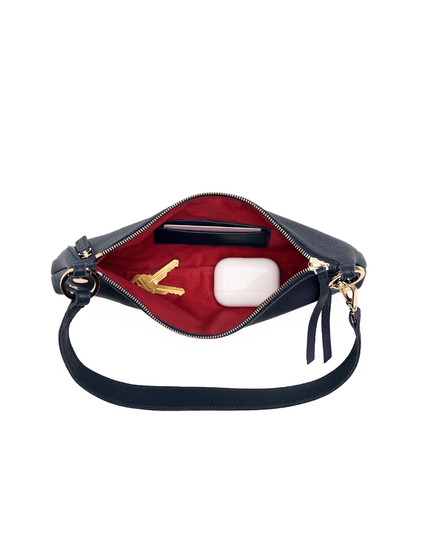 A navy blue shoulder bag shown open, revealing a bright red interior lining. Inside, there is a black card holder, a gold key, and a white wireless earbud charging case.