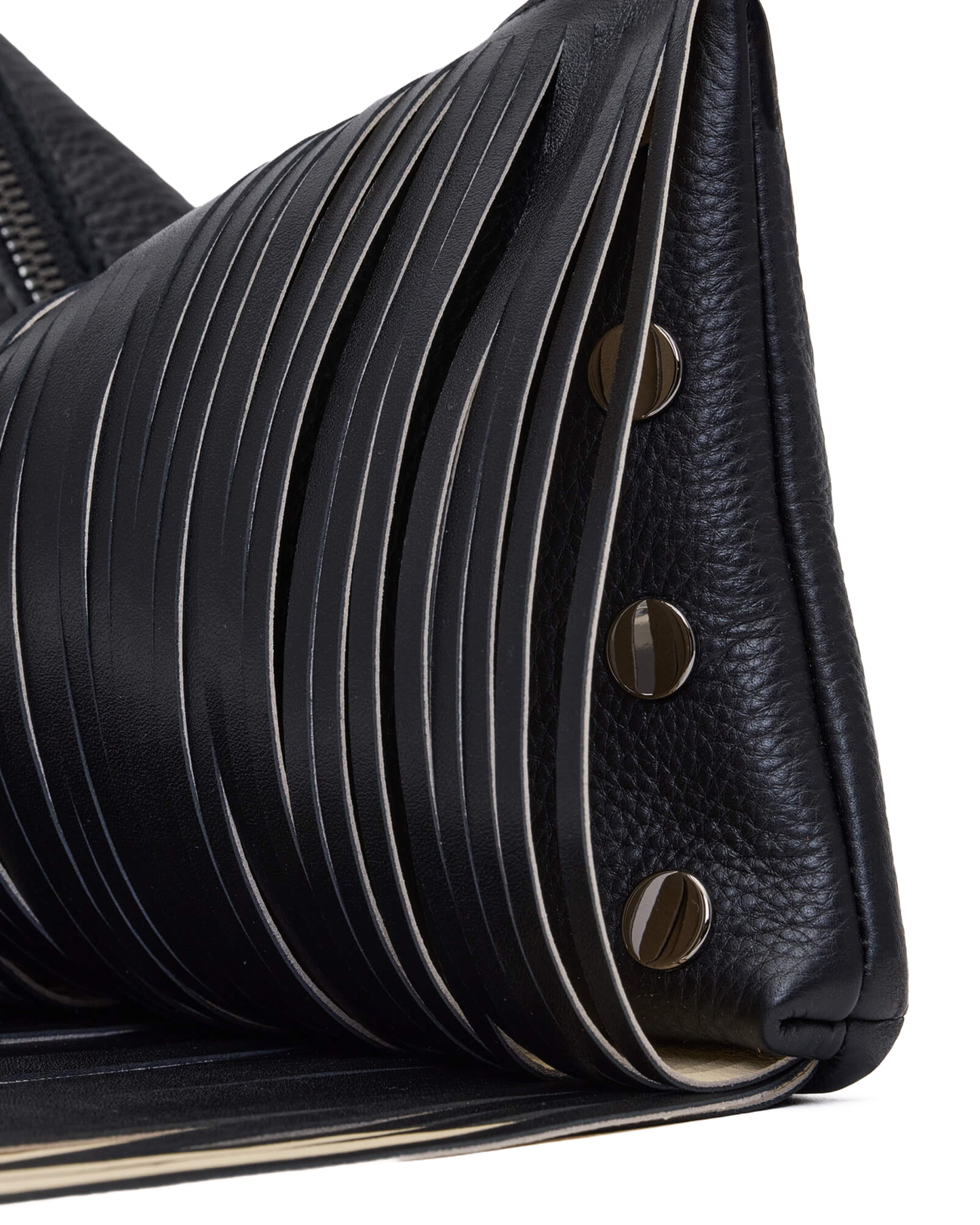 Close-up of a black leather handbag showing pleated and pebbled textures with round metal studs and fringe on a white background.