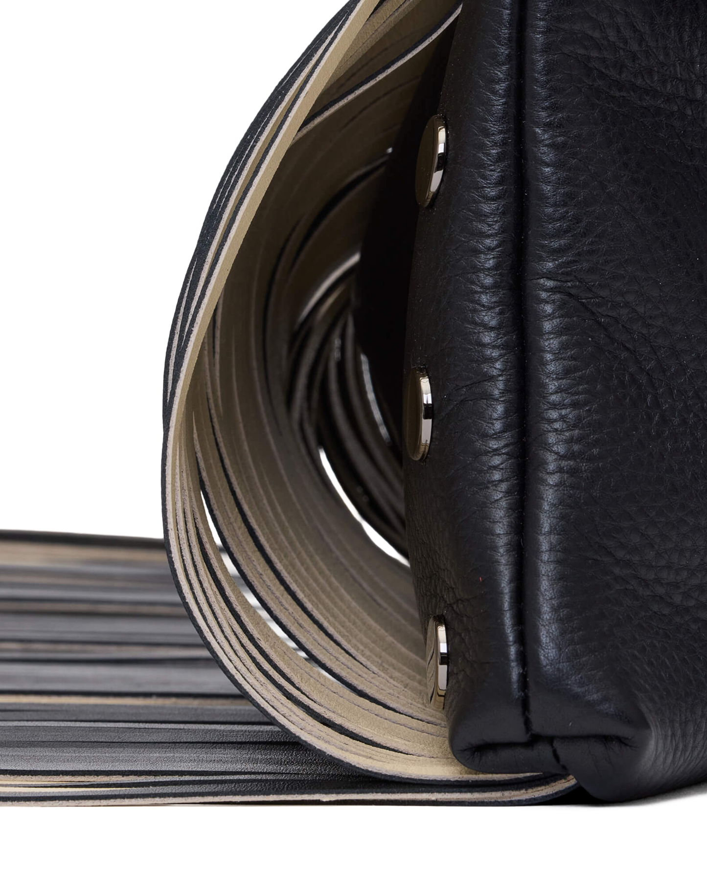 Close-up of a black pebbled leather clutch or small bag with silver-tone metal snap buttons and fringe, showing the space difference between the bag and it's fringe details.