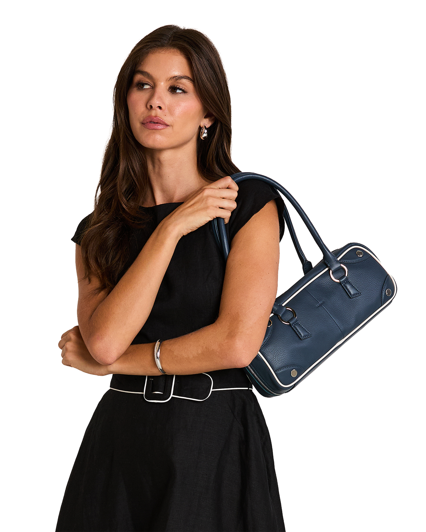 A woman in a black sleeveless top and skirt carries a navy blue leather handbag with white piping and silver hardware.