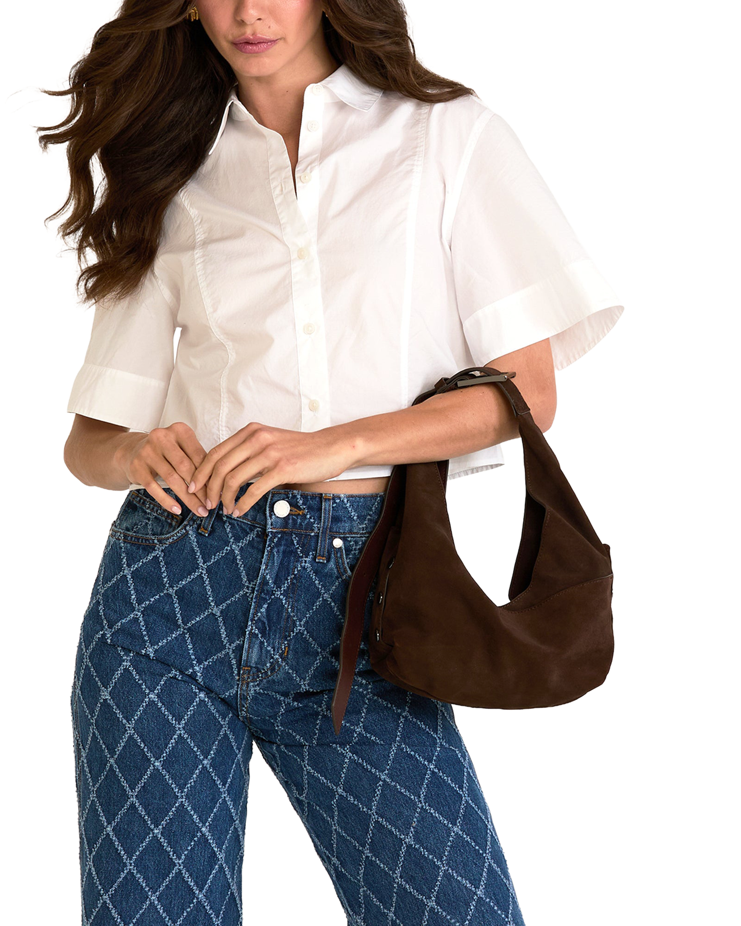 A woman wearing a white short-sleeve button-up shirt and blue patterned jeans, carrying a brown suede shoulder bag.