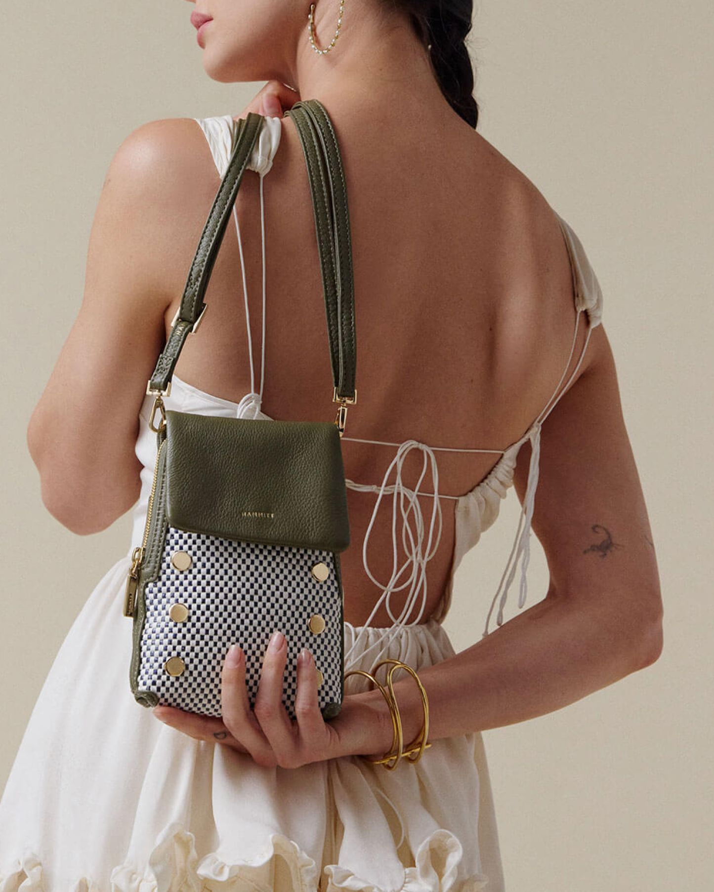 Woman holding a green and black patterned handbag against a neutral background.