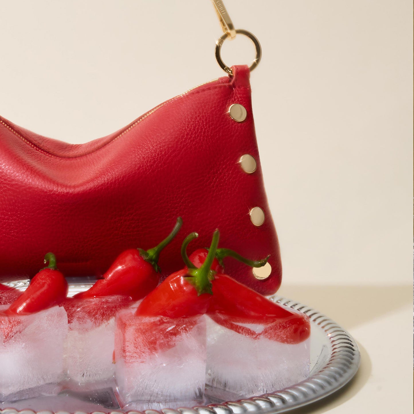 Red leather handbag with gold accents on a tray of ice and red peppers.