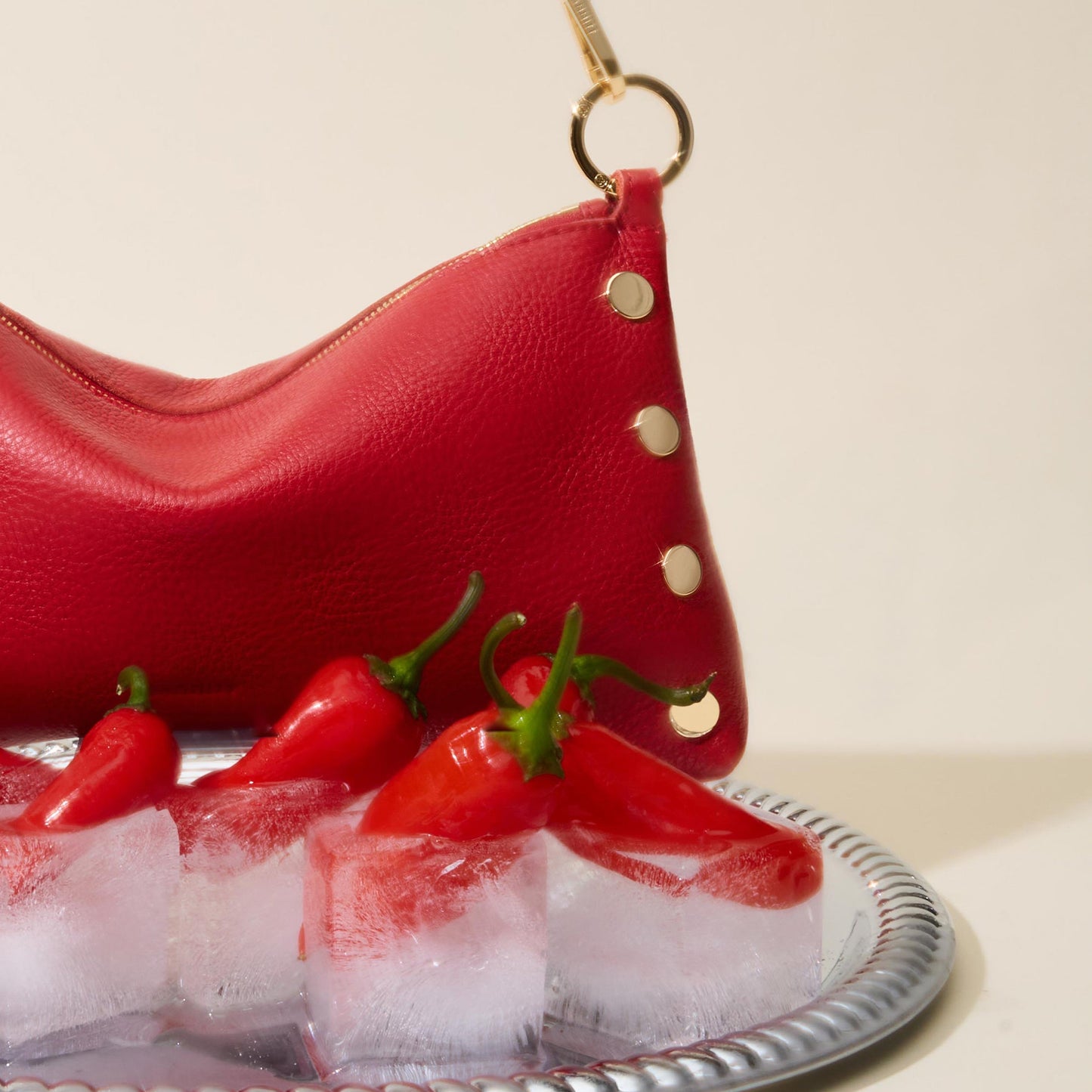 Red leather handbag with gold accents on a tray of ice and red peppers.