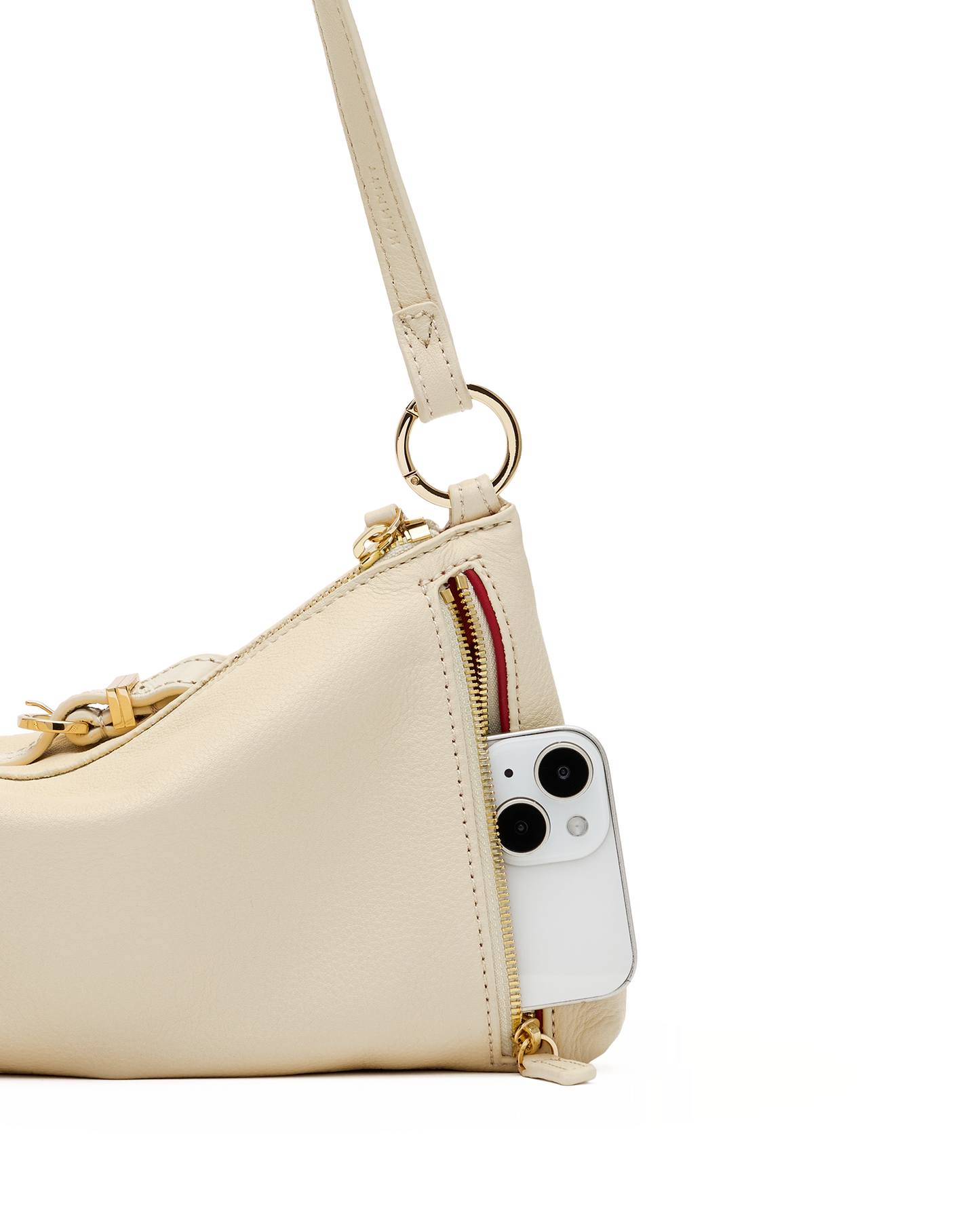 A close-up of a light beige leather shoulder bag with gold-tone hardware, featuring a side zipper pocket containing a white smartphone, set against a plain white background.