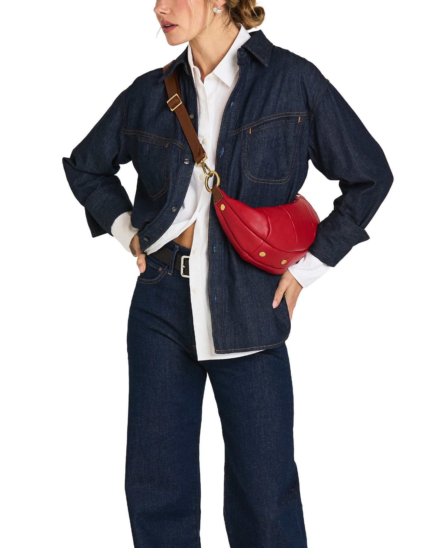 A model wearing a dark indigo denim jacket and matching wide-leg jeans, styled with a white button-down shirt, a black belt, and a bright red leather crescent-shaped crossbody bag with a brown strap and gold hardware.