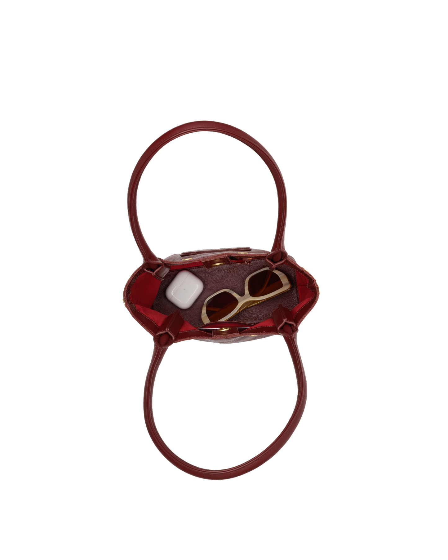 A small glossy burgundy handbag with a top handle, shown from above on a plain white background. Inside the bag, a pair of gold-framed sunglasses and a white rectangular item are partially visible.