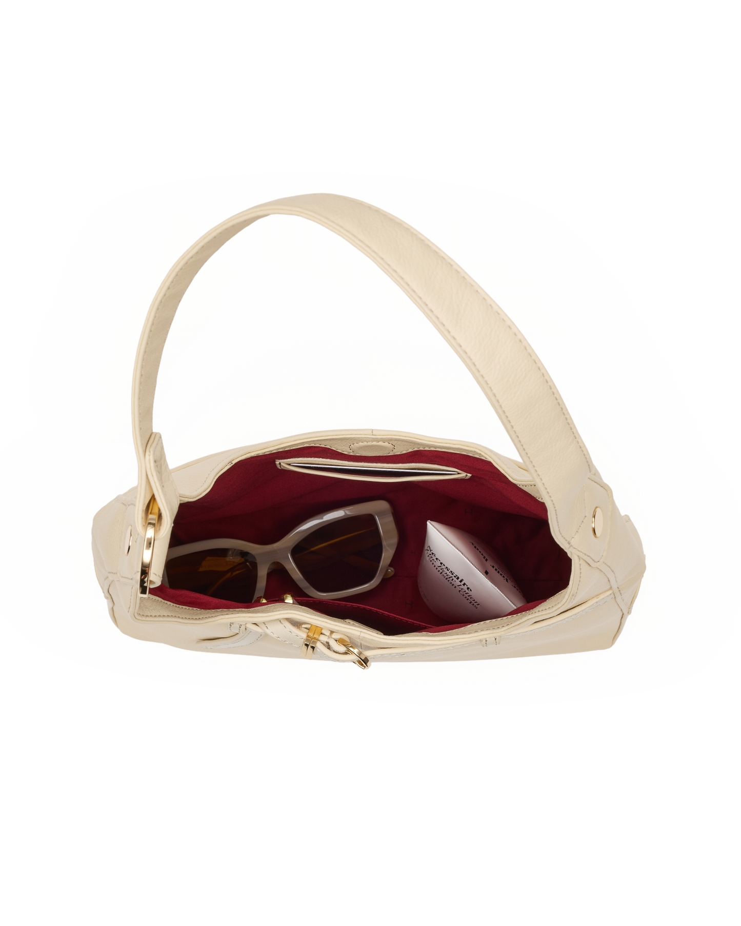 An open cream-colored leather shoulder bag with a burgundy interior, shown against a plain white background. Inside, a pair of sunglasses and a small white cosmetic pouch are visible.