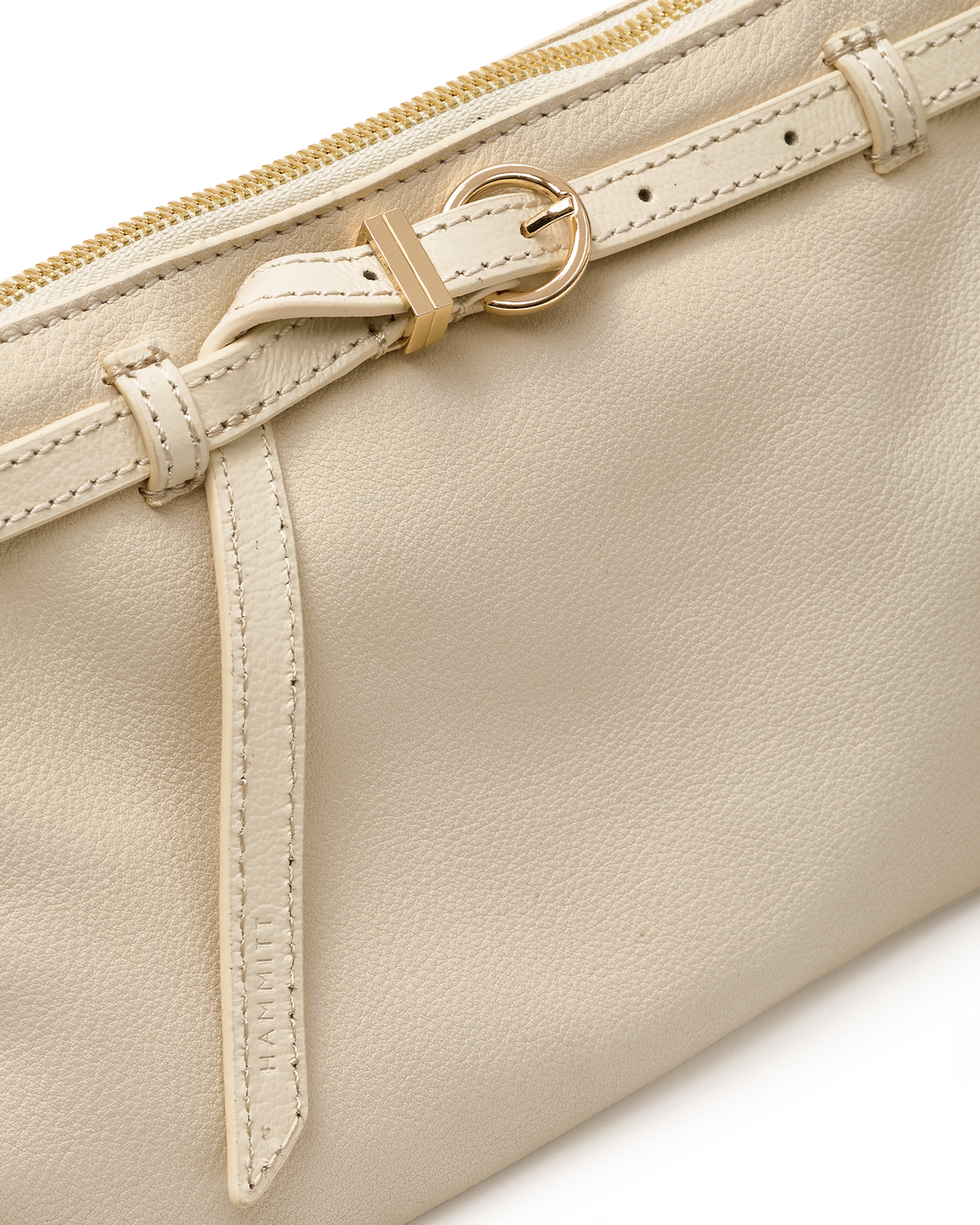 Close-up of a cream-colored leather pouch featuring a matching leather strap with a gold-tone buckle and zipper pull.