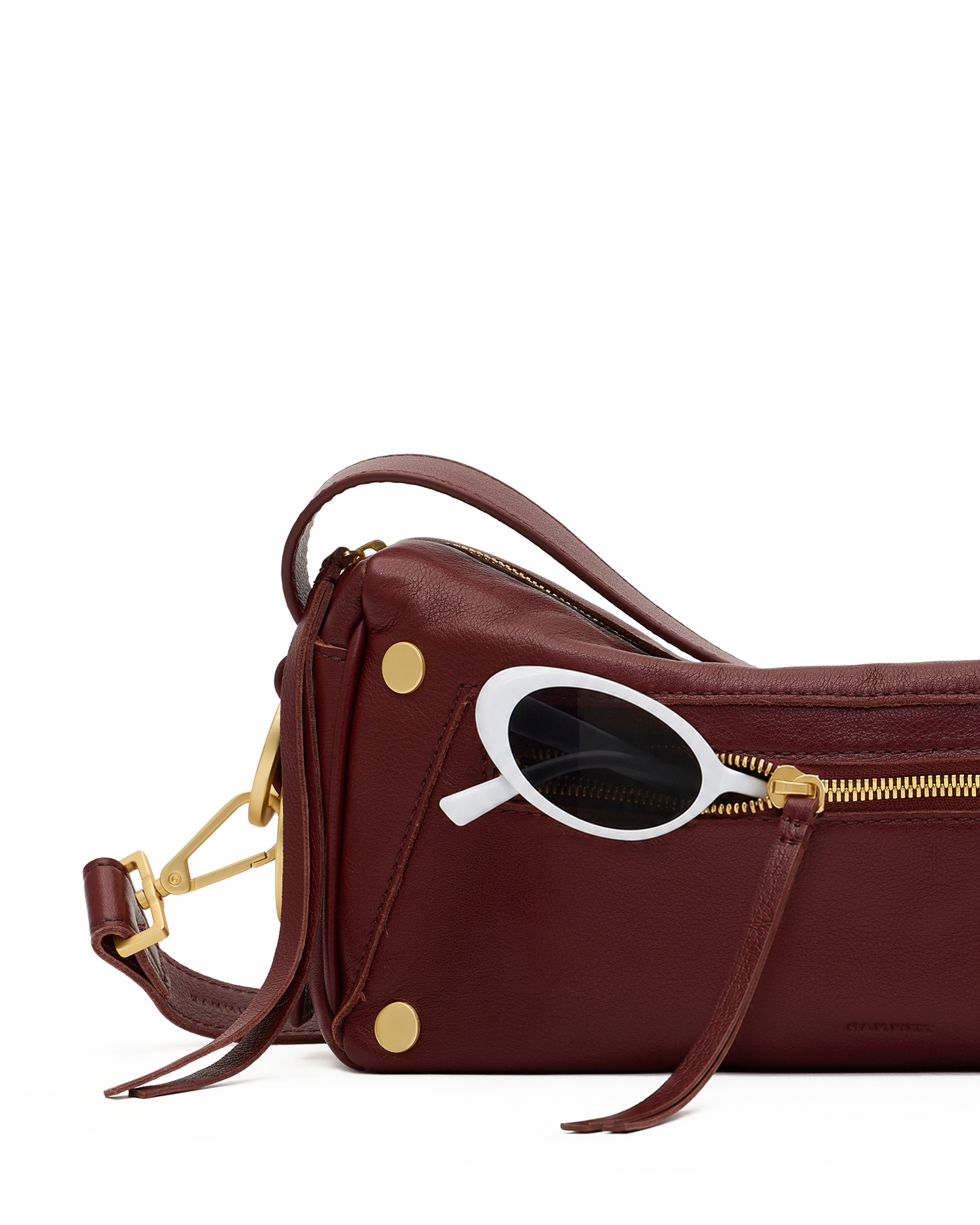 A burgundy leather shoulder bag with gold-tone hardware and a white-framed sunglasses accessory resting on top, shown against a solid white background.