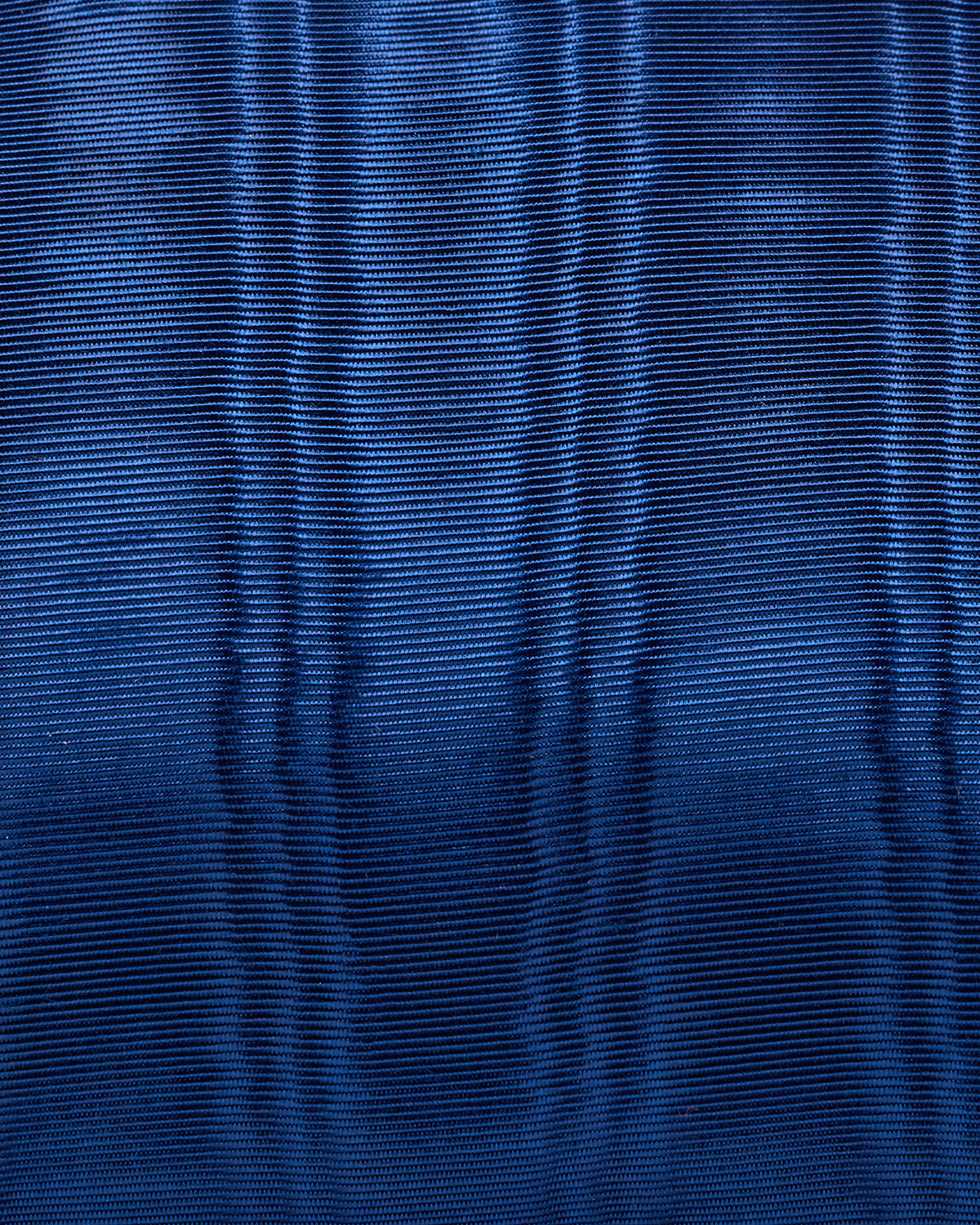 A close-up of a textured royal blue fabric with a fine ribbed or pleated pattern.