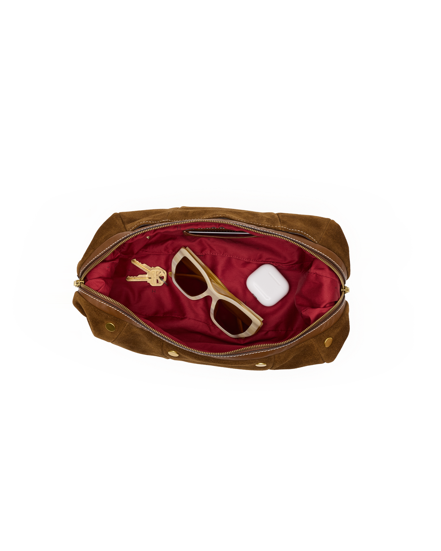 A brown suede cosmetic pouch shown open from above, revealing a deep red satin interior with sunglasses, keys, and a small white item inside. The pouch has gold-tone hardware and is photographed on a plain white background.