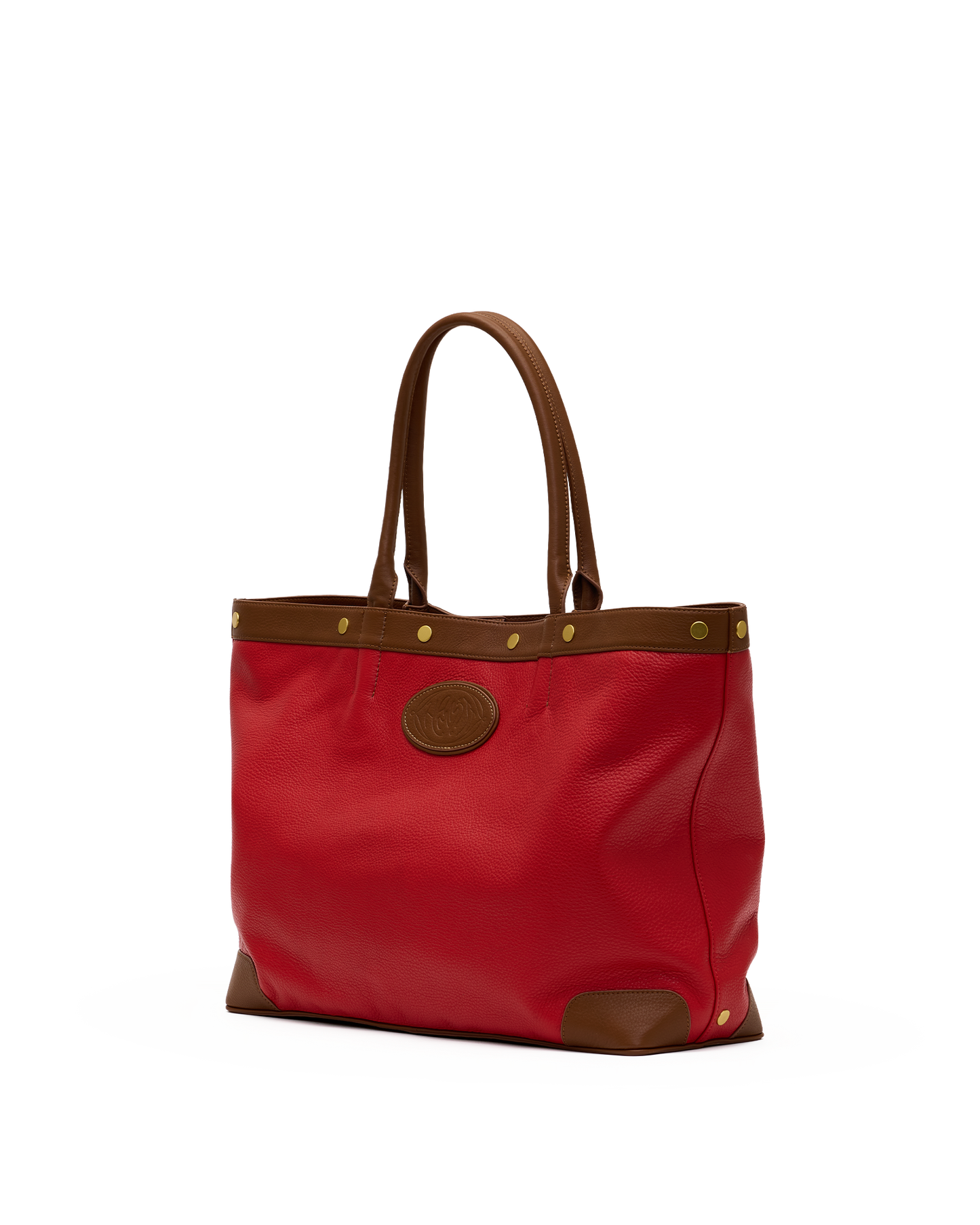 A red tote bag with brown leather handles, trim, and corner protectors, featuring brass-tone hardware and a circular brown logo patch on the front, set against a plain white background.