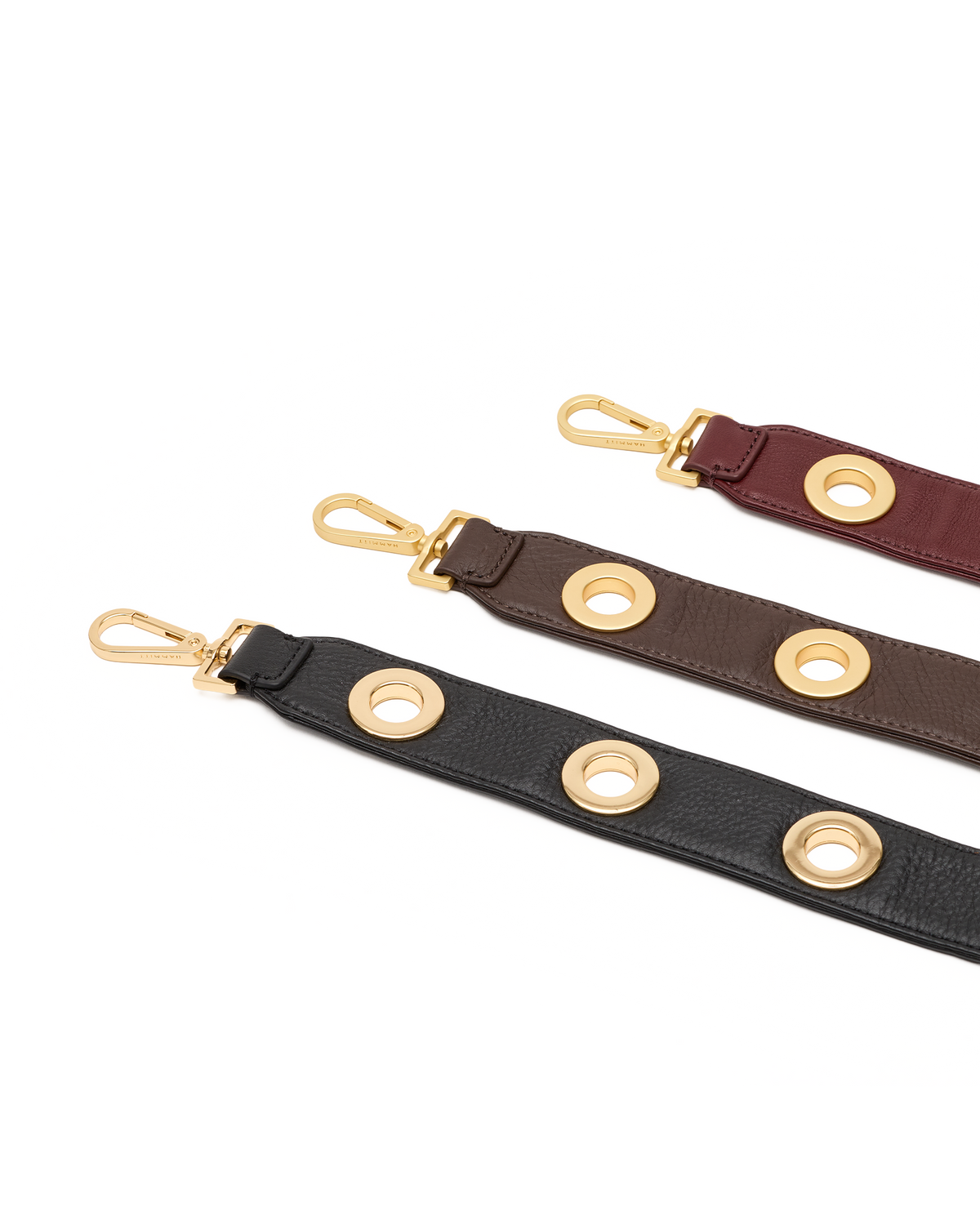 Three leather shoulder straps in black, brown, and burgundy, each featuring gold-tone metal grommets and a swivel snap hook clasp, arranged diagonally on a white background.