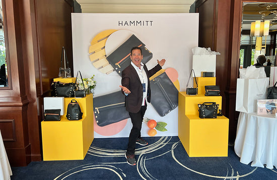 Image of Tony with assortment of Hammitt handbags around him on display.