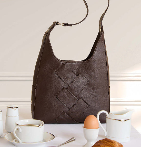 Brown leather handbag with woven pattern on a white surface with tea set