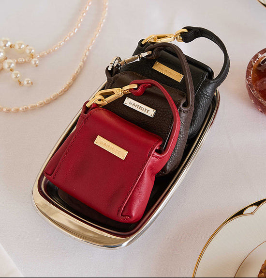 Two small handbags, one red and one black, on a white surface with a gold chain and dish in the background.