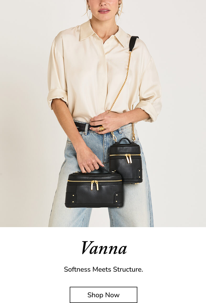 A model wearing a cream button-down shirt and light-wash jeans holds two black structured crossbody bags with gold-tone hardware and chain straps. The image has a white footer with the text 'Vanna', 'Softness Meets Structure.