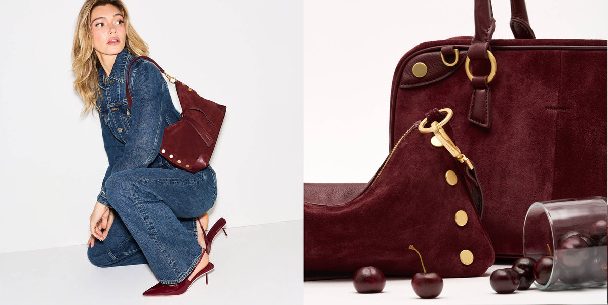 A model in a denim jumpsuit kneels on a white studio floor carrying a burgundy suede shoulder bag with gold hardware. The right side shows a close-up of the same burgundy bag and matching pouch with gold-tone studs and rings, alongside cherries and a glass of cherries.