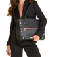 A woman in a black blazer and pants carries a large black leather tote bag with gold-tone studs and a red horizontal zipper accent, photographed against a plain white background.