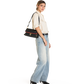 A woman modeling a black shoulder bag with red and gold trim, styled with a cream short-sleeve blouse, light-wash wide-leg jeans, and black pointed-toe heels against a plain white background.
