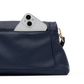 A close-up of a navy blue pebbled leather pouch or clutch with a white smartphone partially tucked into the top pocket, showing a gold-tone ring pull on a white background.