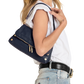A woman wearing a white sleeveless top and light blue jeans carries a navy blue leather shoulder bag with gold-tone hardware against a plain white background.