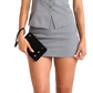 A model wearing a gray two-piece suit with a peplum-style top and matching mini skirt, holding a black clutch purse with silver studs.