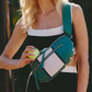 A woman wearing a black and white cutout dress carries a green and white leather crossbody bag with silver studs and zippers, holding a yellow tennis ball.