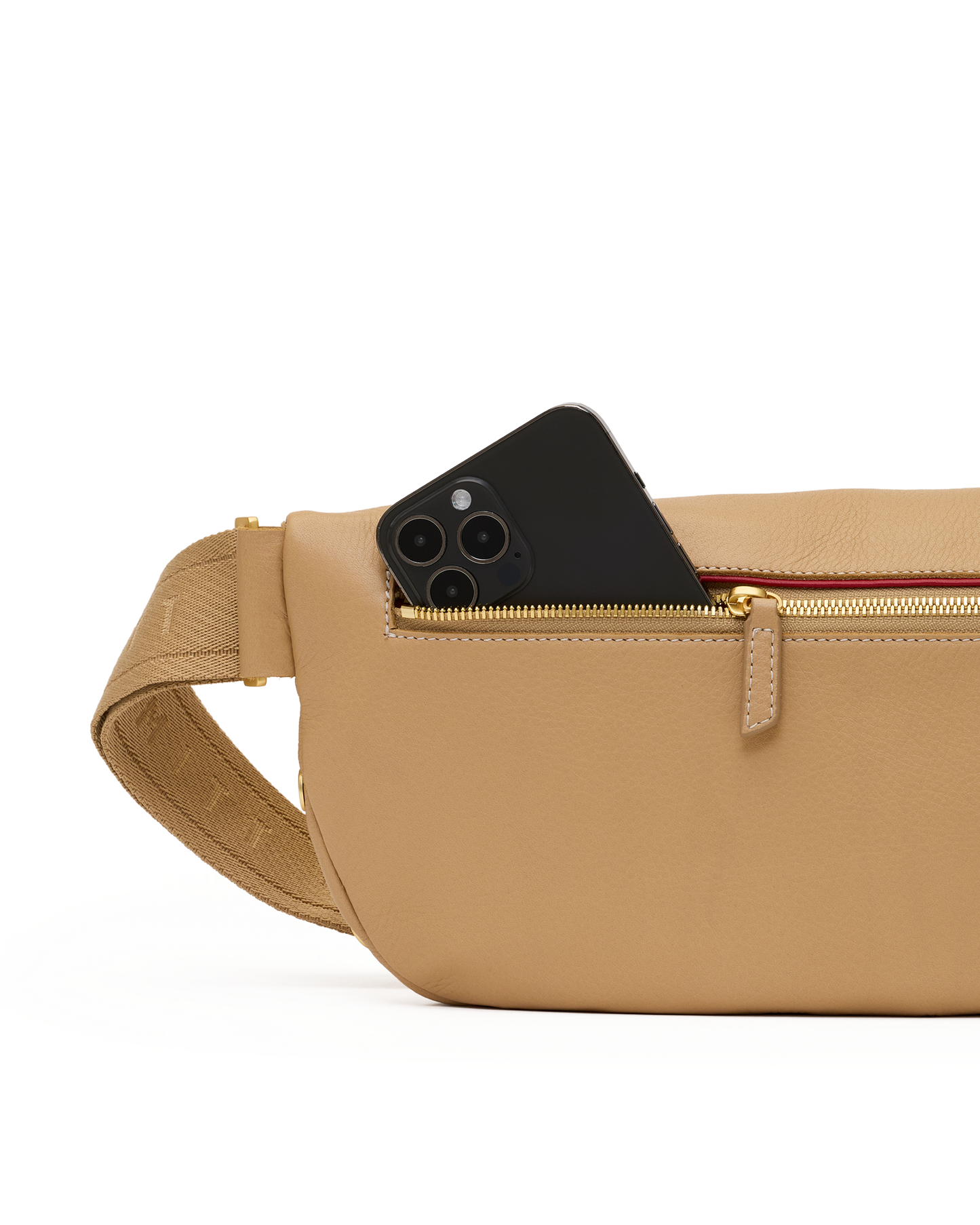 A tan pebbled leather crossbody bag with a gold zipper and a black smartphone partially tucked into the front pocket, shown against a clean white background.