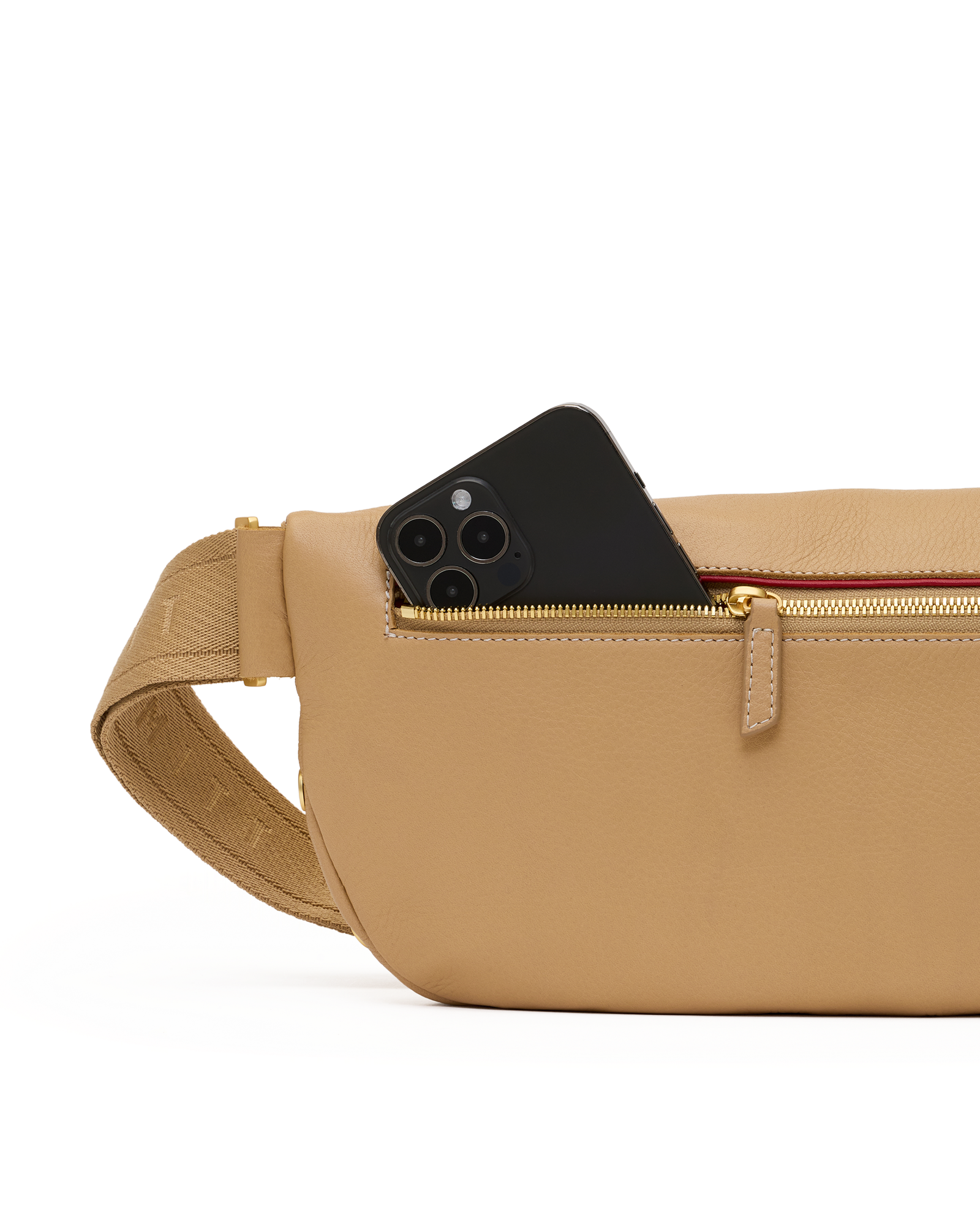 A tan pebbled leather crossbody bag with a gold zipper and a black smartphone partially tucked into the front pocket, shown against a clean white background.