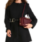 A woman wearing a black long-sleeve coat with a wide belt and holding a burgundy leather shoulder bag, shown against a plain white background.