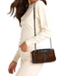 A woman wearing a cream ribbed knit sweater and matching cream pants carries a brown cowhide shoulder bag with dark leather trim and a silver chain strap.