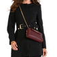 A woman wearing a black longline coat with a matching belt and a burgundy leather crossbody handbag with a gold chain strap.