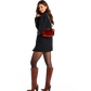 A woman modeling a black mini dress, black tights, and brown knee-high heeled boots, carrying a red textured shoulder bag.