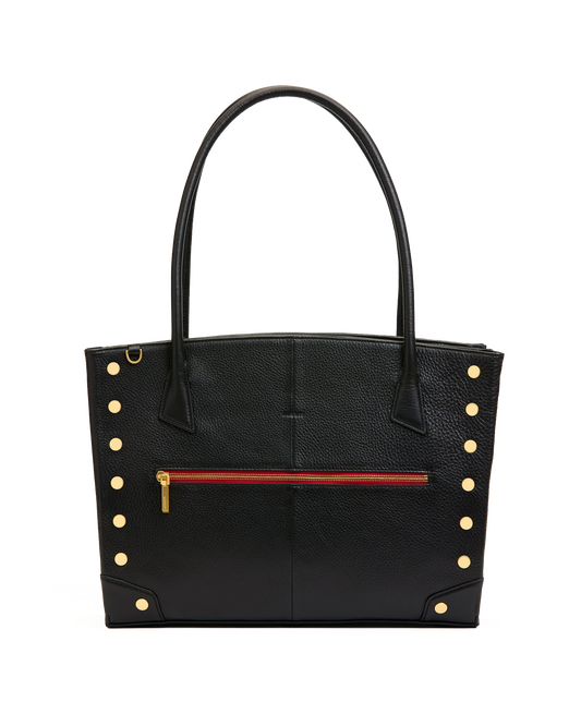 A black pebbled leather tote bag with double top handles, gold-tone rivet studs on the sides, and a horizontal red zipper pocket on the front.