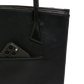 Close-up of a black pebbled leather tote bag with a side pocket holding a dark smartphone, shown against a plain white background.