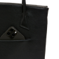 Close-up of a black pebbled leather tote bag with a side pocket holding a black smartphone, on a white background.