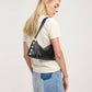A blonde woman wearing a cream t-shirt and a denim patchwork mini skirt, shown from a side-back angle while wearing a black leather shoulder bag with gold-tone studs and a strap.