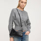 A woman wearing a gray button-front knit sweater and blue jeans, carrying a black leather shoulder bag with silver-tone hardware against a light gray studio background.