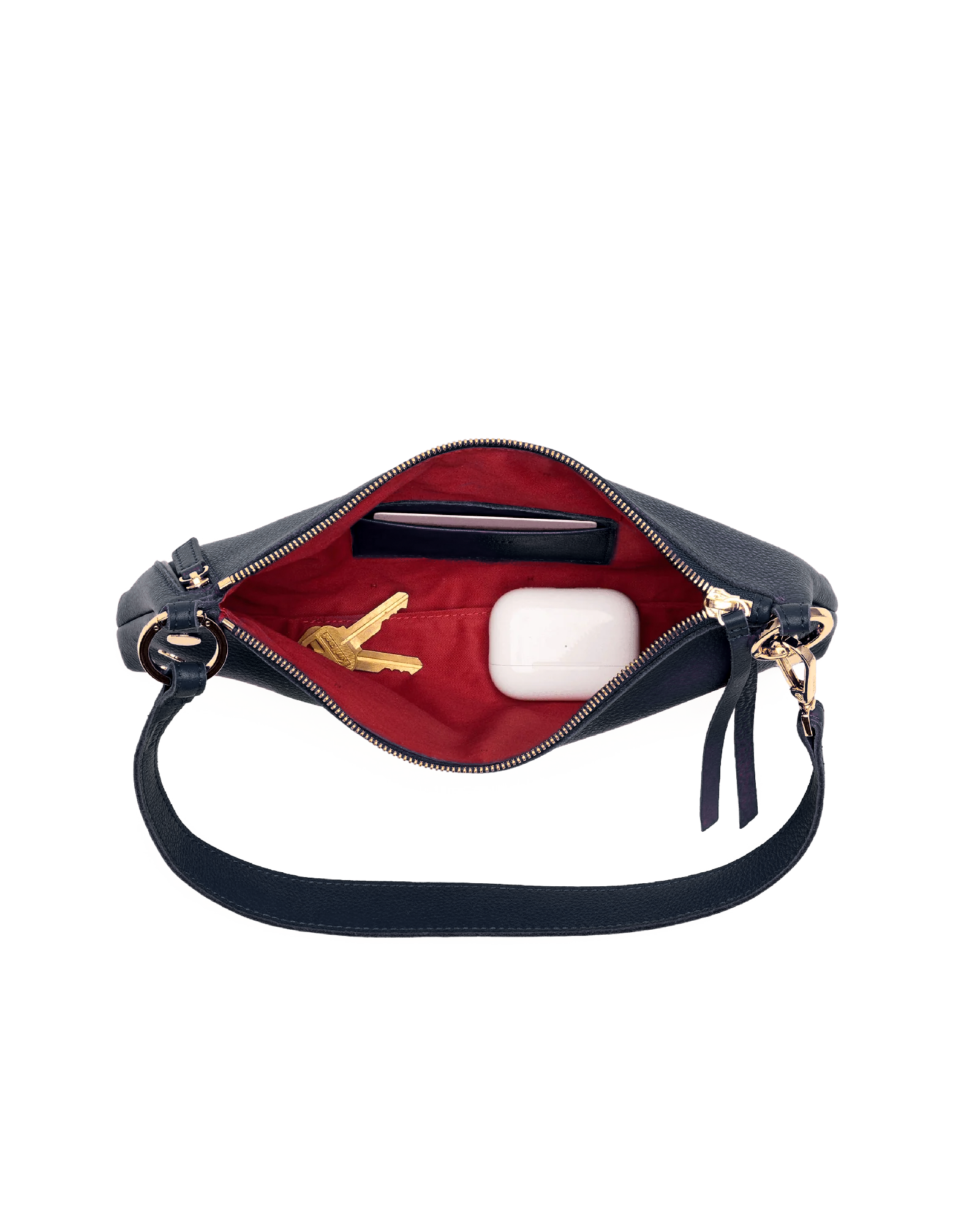 A navy blue shoulder bag shown open, revealing a bright red interior lining. Inside, there is a black card holder, a gold key, and a white wireless earbud charging case.