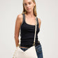 A woman modeling a cream-colored shoulder bag with gold-tone hardware and a matching strap, styled with a black tank top and blue jeans against a light gray studio background.
