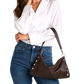 A woman wearing a white button-up blouse and blue jeans carries a dark brown leather shoulder bag with silver-tone studs and a wide strap.