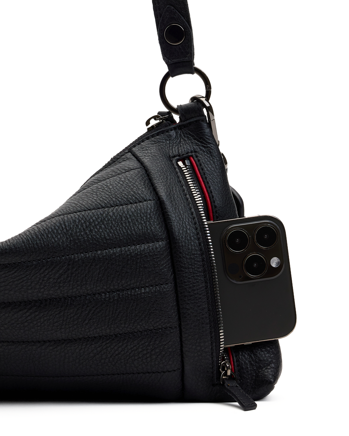 A close-up of a black pebbled leather shoulder bag with a side zipper, shown with a black smartphone tucked into the zip pocket. The bag has a quilted texture and a black strap, photographed on a solid white background.