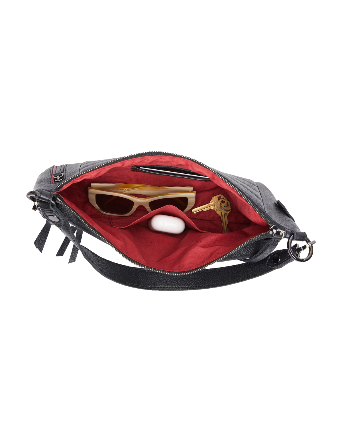An open black leather shoulder bag with a bright red interior lining, shown against a plain white background. Inside, the bag contains sunglasses, keys, a white earbud case, and a slim black accessory.