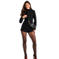 A woman modeling a black textured long-sleeve mini jacket and matching shorts set, styled with sheer black tights, red high heels, and a small black shoulder bag with gold hardware.