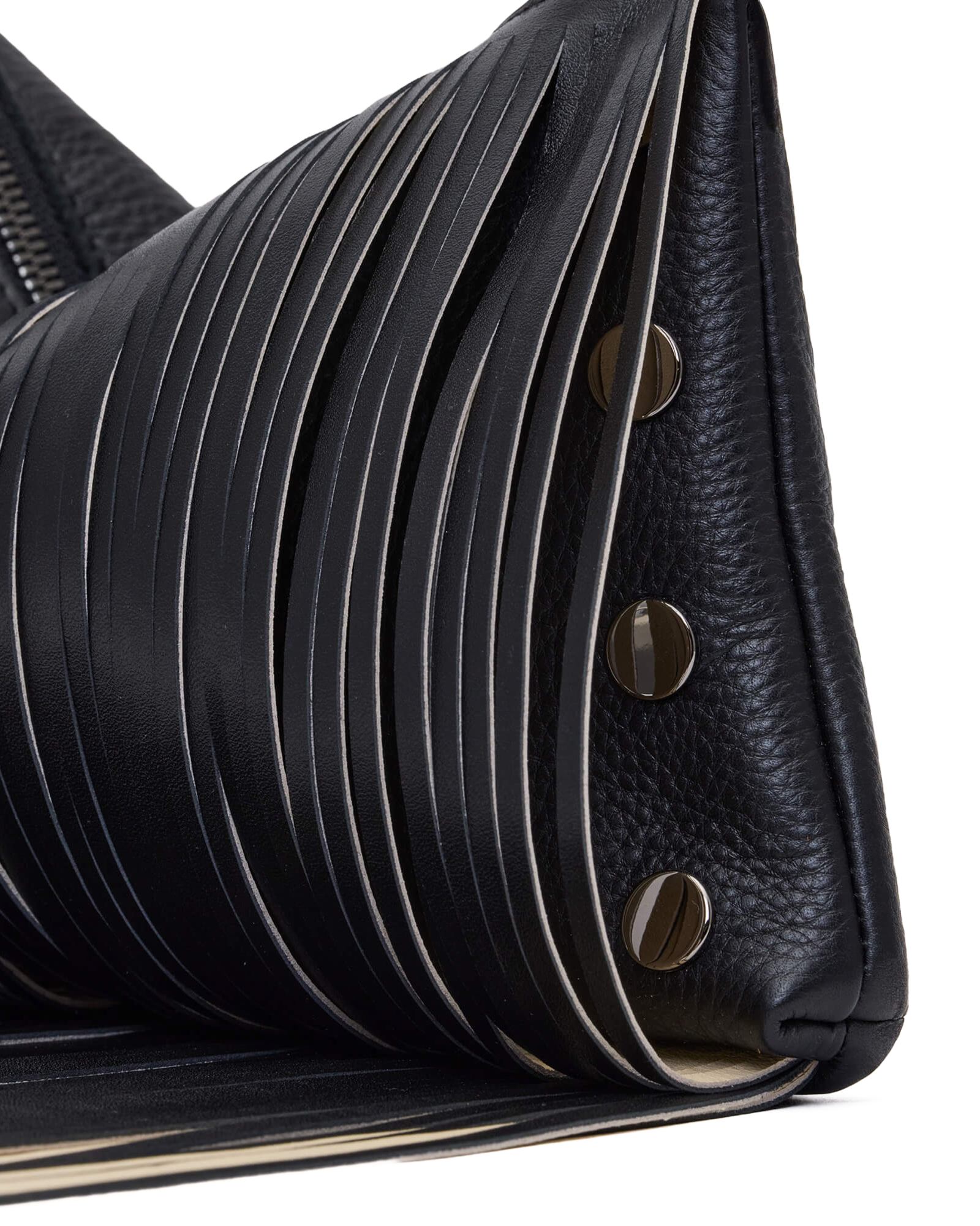 Close-up of a black leather handbag showing pleated and pebbled textures with round metal studs and fringe on a white background.